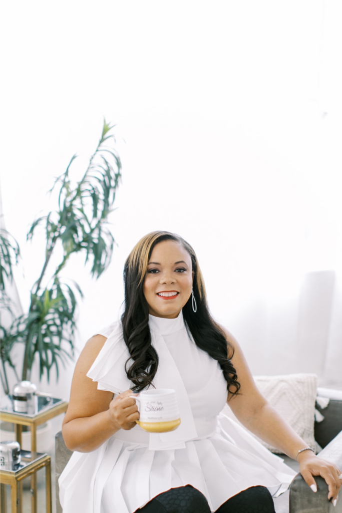 Marshecka Rodgers, luxury wedding and event planner, seated gracefully in an ivory-toned setting, wearing a chic black outfit with soft curls and a poised expression — embodying elegance, intention, and timeless style.