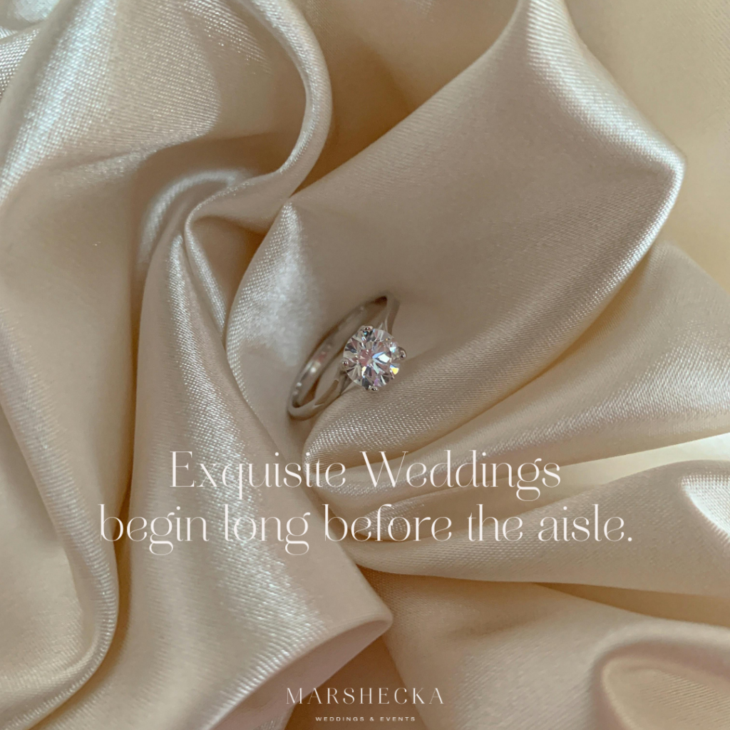A soft editorial image featuring a solitaire engagement ring placed on champagne satin fabric. Overlaid text reads “Exquisite Weddings Begin Long Before the Aisle,” representing Marshecka Weddings & Events and their approach to elegant, full-service wedding planning for discerning couples worldwide.