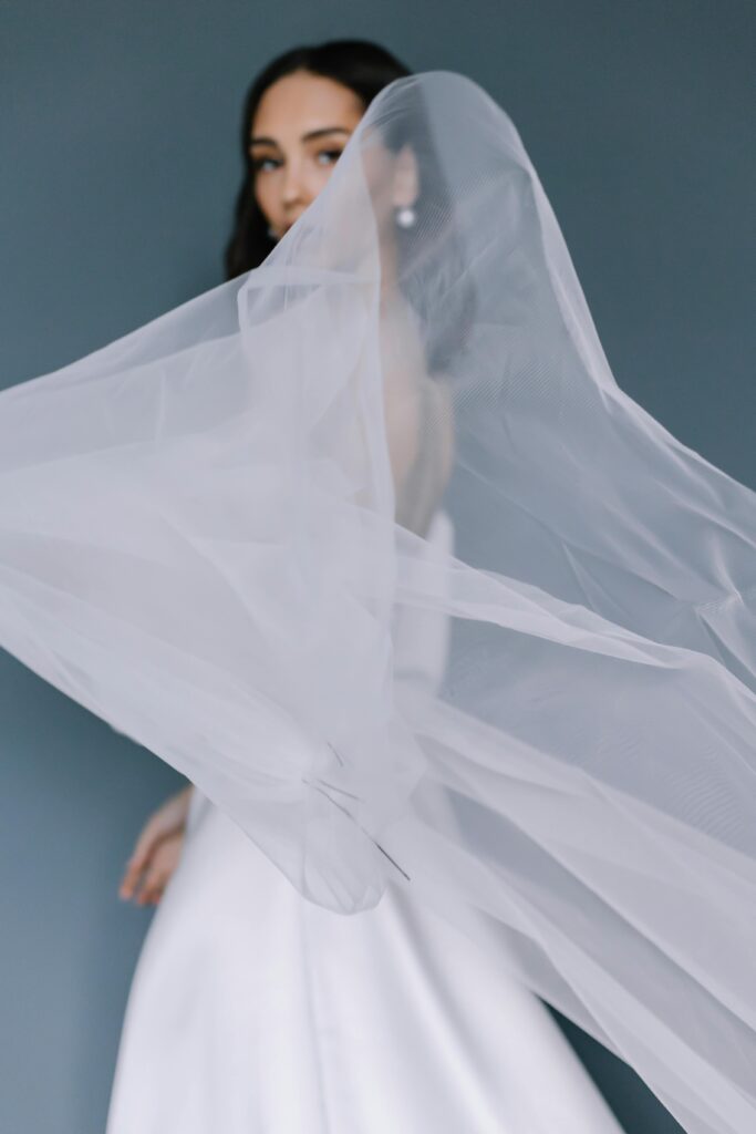 Bride in a white gown with her veil flowing across the frame, creating a soft and ethereal visual moment that reflects timeless elegance.