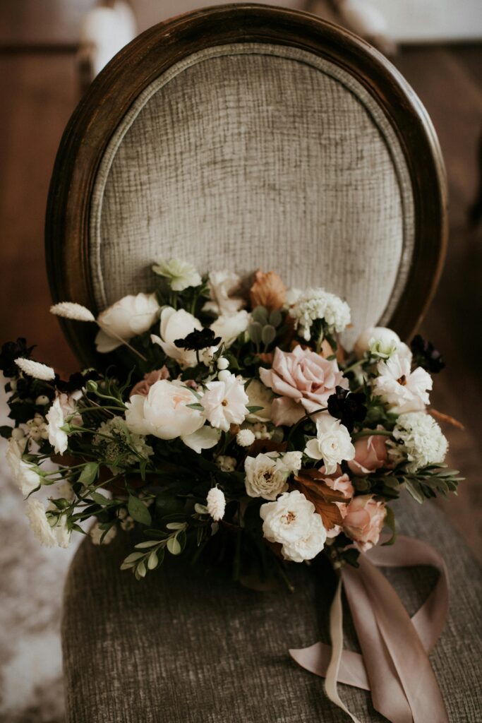 Elegant blush bouquet resting on vintage velvet chair, representing intentional design and immersive guest experience in a luxury wedding setting.