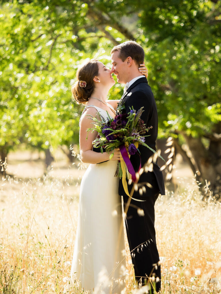 Luxury wedding couple sharing an intimate moment outdoors, with elegant bridal bouquet and golden sunlight creating a timeless, romantic atmosphere.