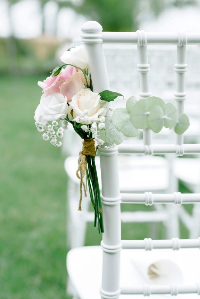 Elegant white chiavari chair adorned with soft blush and ivory roses, symbolizing the ceremony moment where love takes center stage at a luxury wedding.