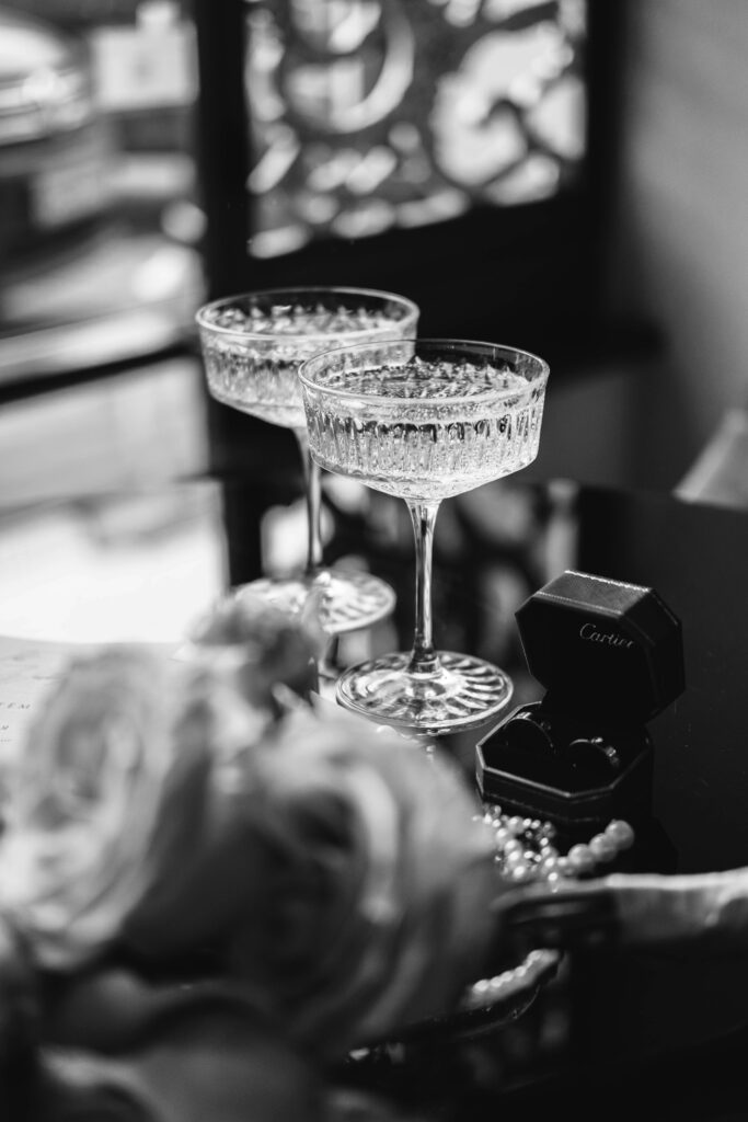 Two crystal champagne glasses with bubbles, Cartier ring box, and roses in black and white, symbolizing refined guest experience at a luxury wedding.