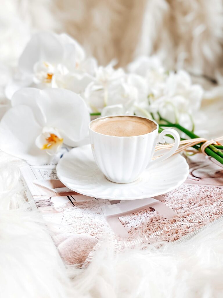 Elegant flat lay of a scalloped white teacup with orchids and editorial textures, styled in a soft neutral setting.