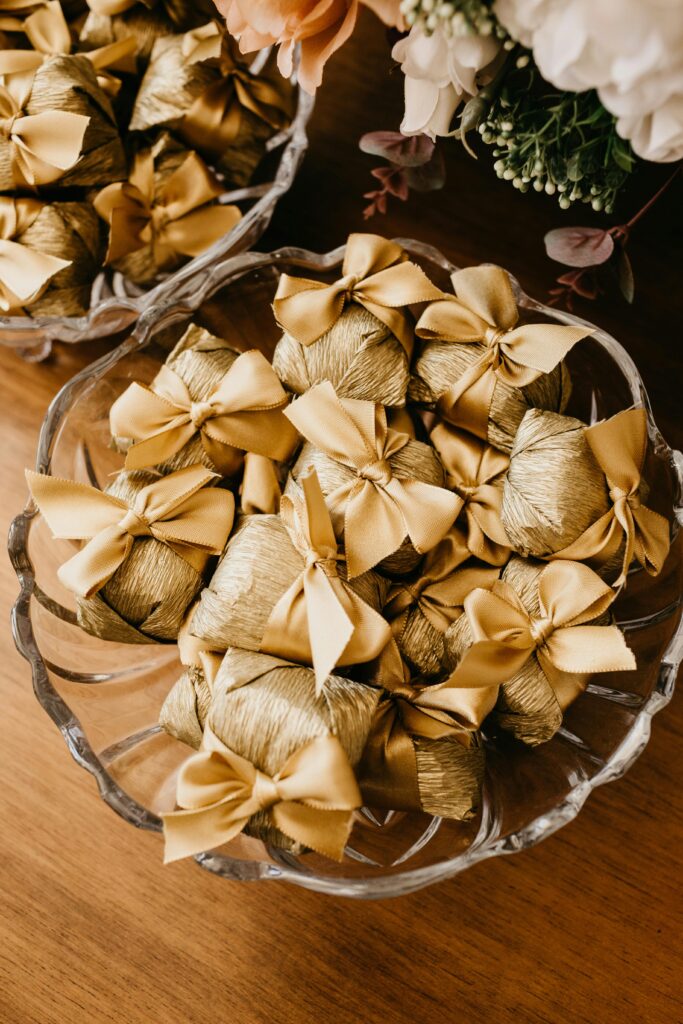 Gold-wrapped wedding favors tied with satin ribbon displayed in glass bowls.