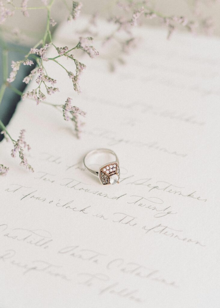 Heirloom-inspired engagement ring on handwritten wedding stationery with soft florals.